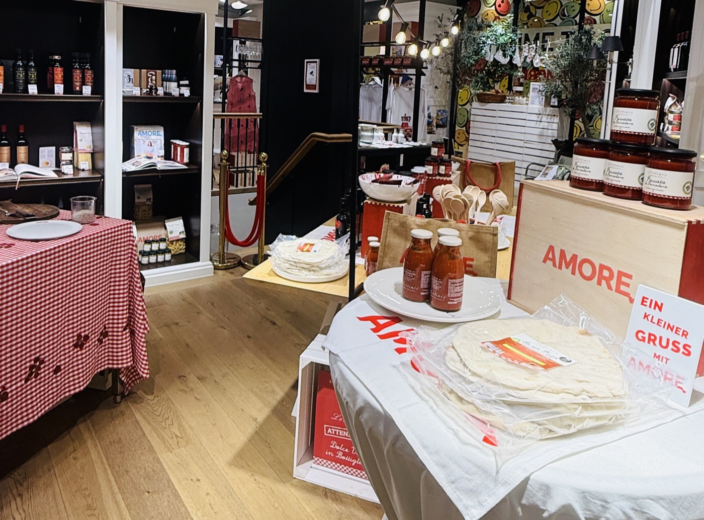 Blick ins Lettinis-Pop-up in der Kö-Galerie Düsseldorf: Probiertische mit Passata, Pizzaböden und Amore-Holzkisten, dahinter Regale mit Wein, Pasta und Kochbüchern